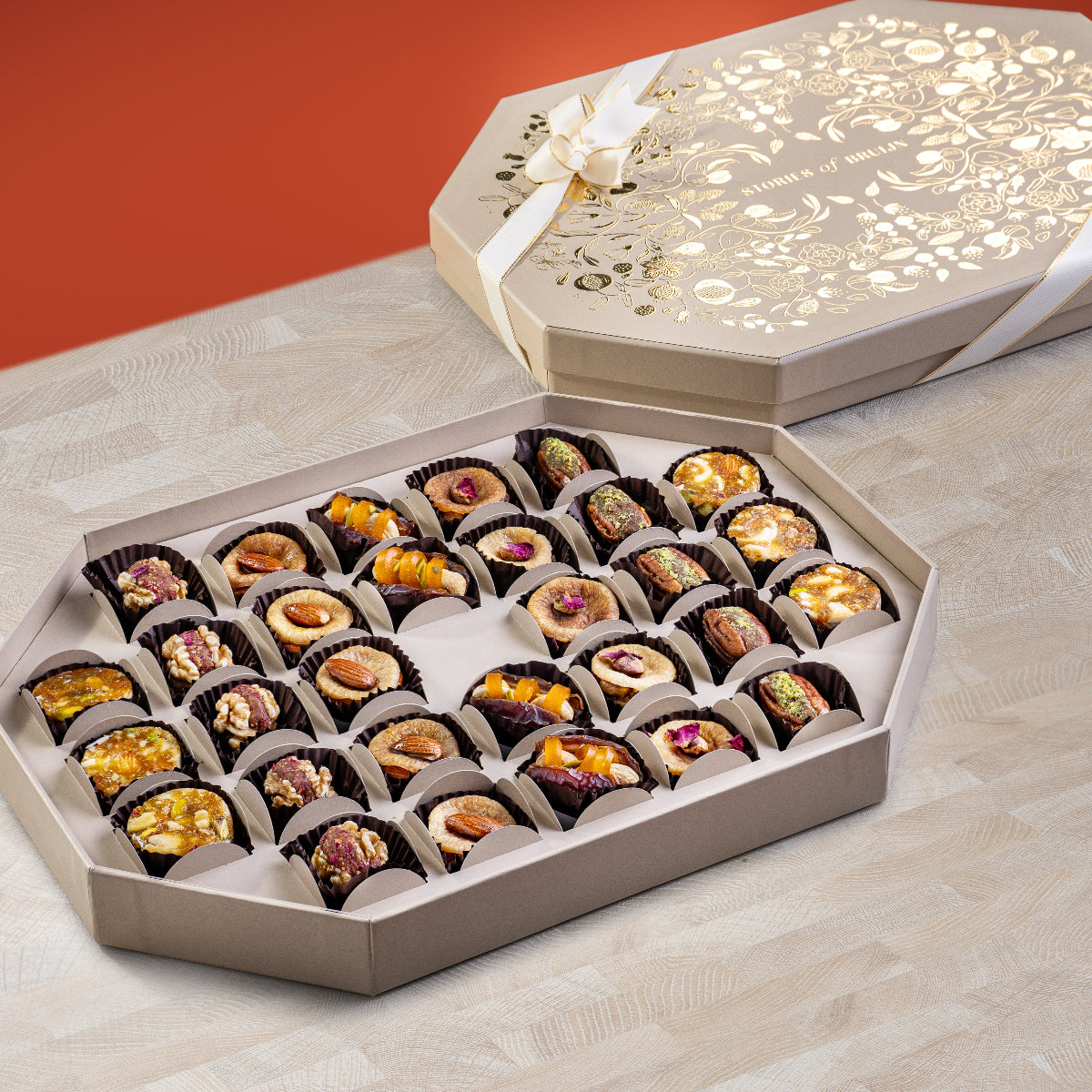 Cream Ruby Box with gold floral design and ribbon, containing an assortment of stuffed dates, fig bites, nut wholes, and saffron rose figs arranged in an elegant tray.