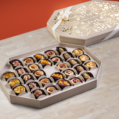 Cream Ruby Box with gold floral design and ribbon, containing an assortment of stuffed dates, fig bites, nut wholes, and saffron rose figs arranged in an elegant tray.