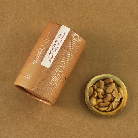 Golden cylindrical container of Bruijn Black Truffle Peanuts placed beside a small bowl of peanuts coated in Italian black truffle seasoning.