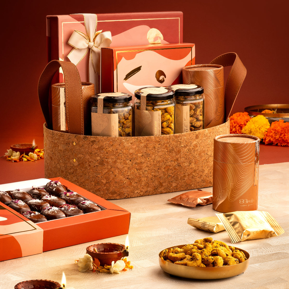 Celebratory Basket with candid box of fig & apricot nut bites, petite paan bites box, cylinders of nut delights, apple chips, and flavored nut jars.