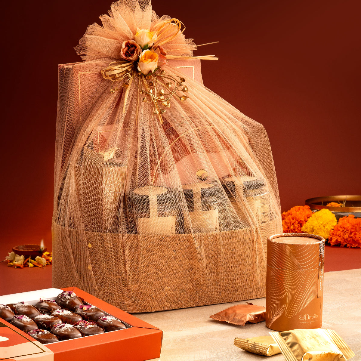 Celebratory Basket with candid box of fig & apricot nut bites, petite paan bites box, cylinders of nut delights, apple chips, and flavored nut jars.