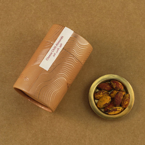 Golden cylindrical container of Bruijn Cheese & Chilli Almonds placed beside a small bowl of almonds coated in cheese and chilli seasoning.