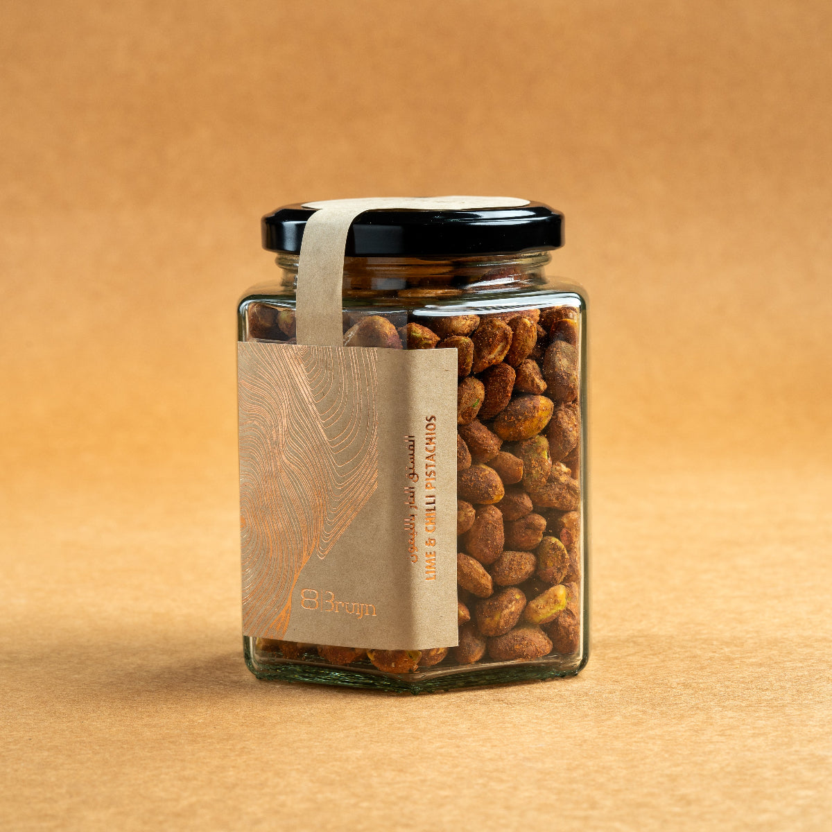 Glass jar of Bruijn Persian Lime & Chilli Pistachios with black lid and kraft label, filled with spiced pistachios coated in lime and chilli seasoning.
