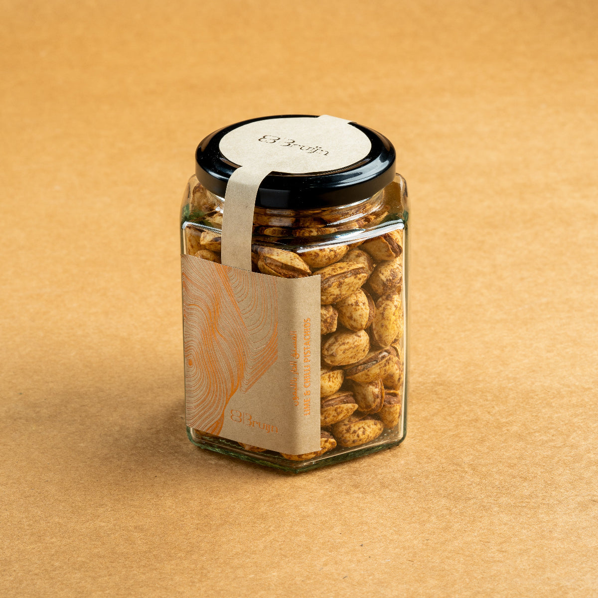Glass jar of Bruijn Persian Lime & Chilli Pistachios with black lid and kraft label, filled with spiced pistachios coated in lime and chilli seasoning.