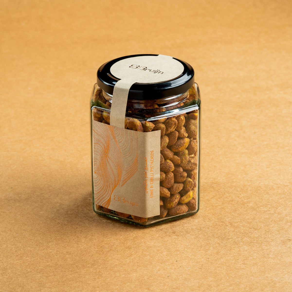 Glass jar of Bruijn Persian Lime & Chilli Pistachios with black lid and kraft label, filled with spiced pistachios coated in lime and chilli seasoning.