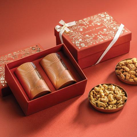 Red Stories of Bruijn gift box with white ribbon, containing two golden cylindrical containers and bowls of Za’atar cashews and Cheese & Chilli Almonds.