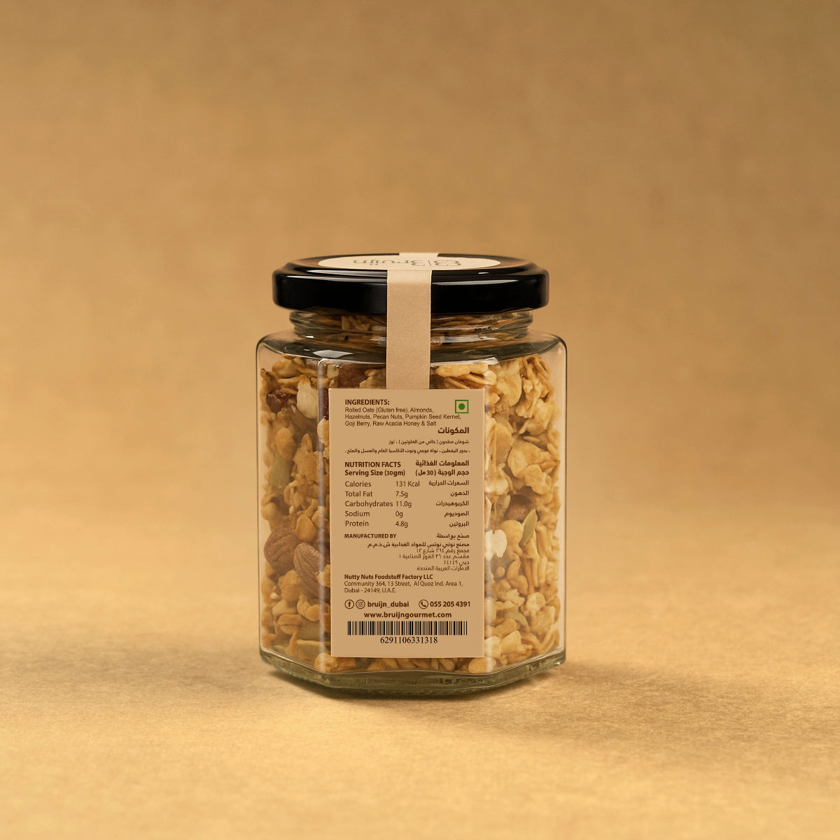 Glass jar of Bruijn Granola with black lid and kraft label, filled with rolled oats, almonds, hazelnuts, pumpkin seeds, and goji berries mixed with honey.