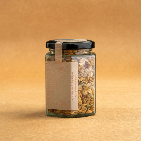 Glass jar of Bruijn Granola with black lid and kraft label, filled with rolled oats, almonds, hazelnuts, pumpkin seeds, and goji berries mixed with honey.