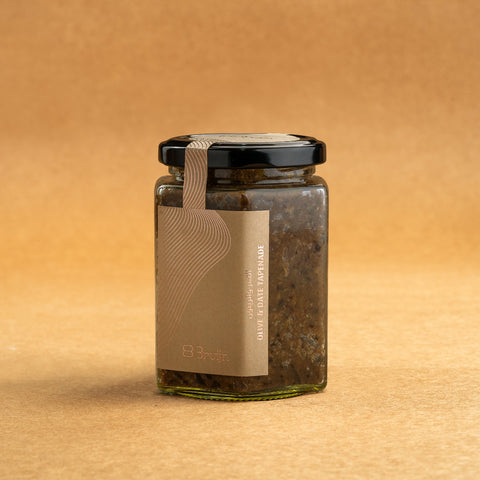 Glass jar of Bruijn Olive & Date Tapenade with black lid and kraft label, containing a dark, rich spread made from sun-dried black olives and dates.