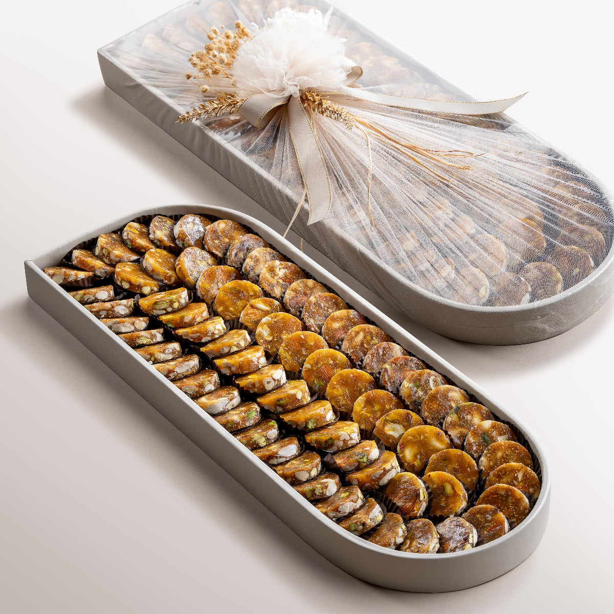 Large oval tray with neatly arranged fig and apricot nut bites. Elegant oval tray wrapped with sheer fabric and floral embellishment for gifting.