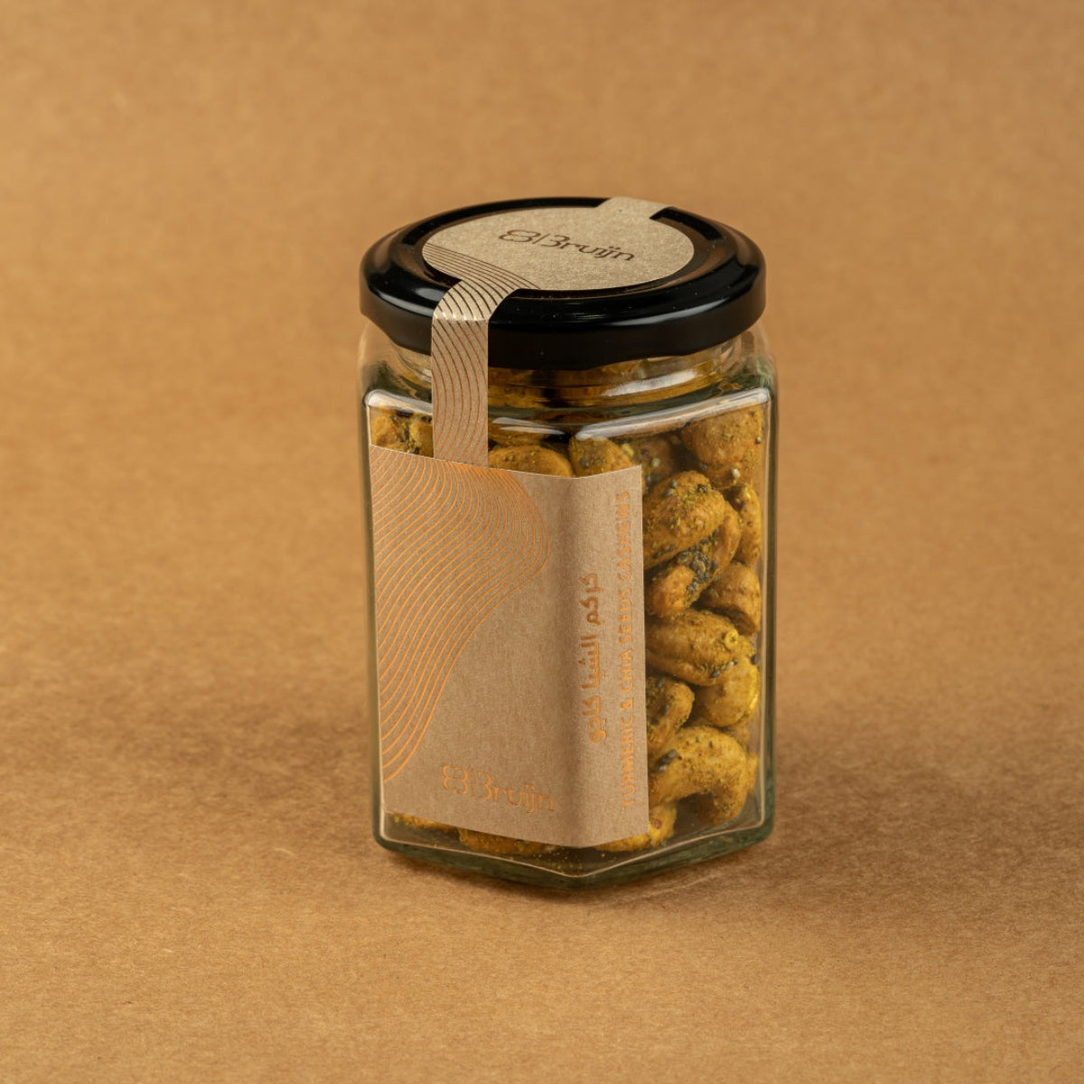 Glass jar of Bruijn Turmeric & Chia Seed Cashews with black lid and kraft label, filled with golden turmeric-coated cashews speckled with chia seeds.
