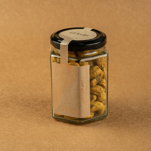 Glass jar of Bruijn Turmeric & Chia Seed Cashews with black lid and kraft label, filled with golden turmeric-coated cashews speckled with chia seeds.