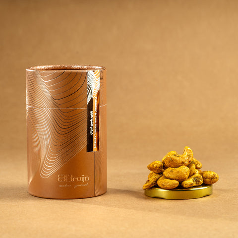 Brown cylindrical container of Bruijn Turmeric & Chia Seed Cashews with minimalist design, containing golden turmeric-coated cashews speckled with chia seeds.