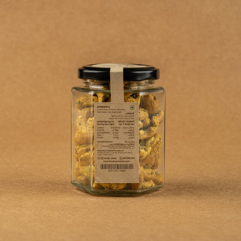 Glass jar of Bruijn Turmeric & Chia Seed Cashews with black lid and kraft label, filled with golden turmeric-coated cashews speckled with chia seeds.