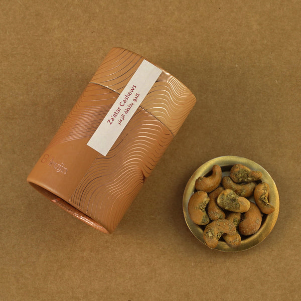 Golden cylindrical container of Bruijn Za’atar Cashews placed beside a small bowl of cashews coated in aromatic Za’atar spice blend.