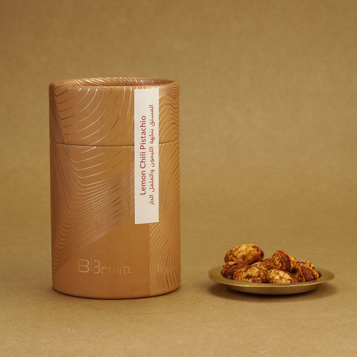 Brown cylindrical container of Bruijn Persian Lime & Chilli Pistachios with minimalist design, containing pistachios coated in tangy lime and spicy chilli seasoning.