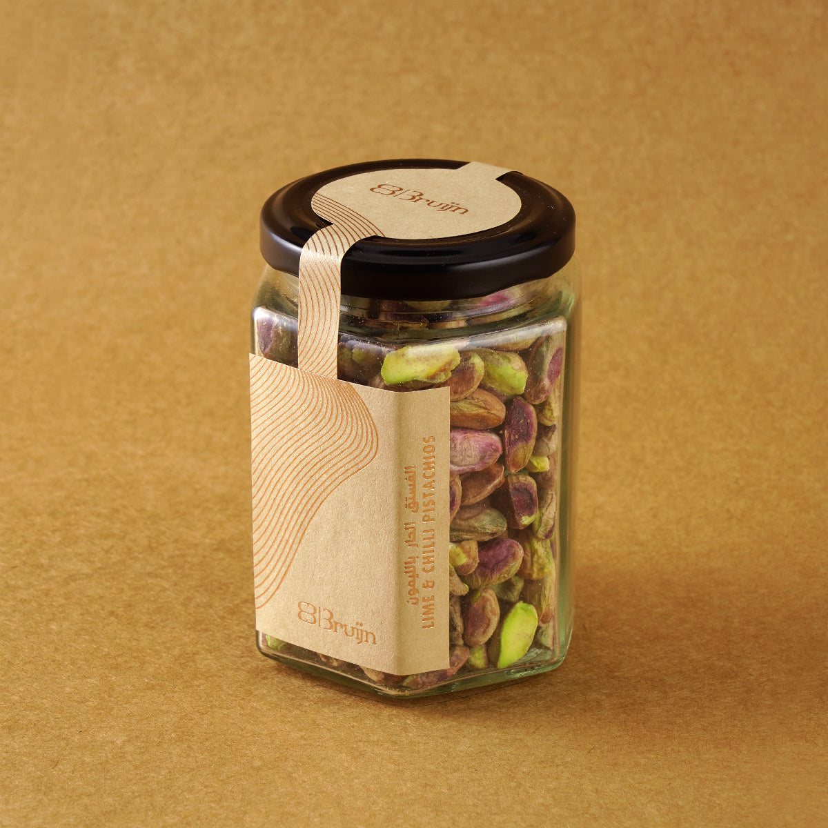 Glass jar of Bruijn Persian Lime & Chilli Pistachios with black lid and kraft label, filled with spiced pistachios coated in lime and chilli seasoning.