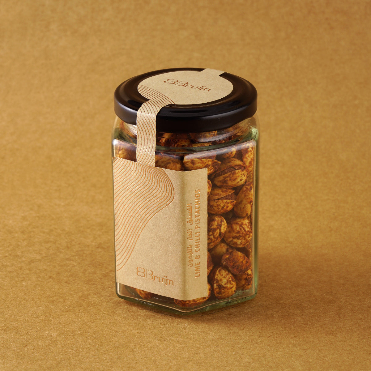 Glass jar of Bruijn Persian Lime & Chilli Pistachios with black lid and kraft label, filled with spiced pistachios coated in lime and chilli seasoning.